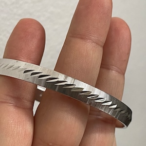 May include: A silver bangle bracelet with a textured, diamond-shaped pattern.