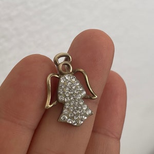 May include: A gold angel charm with clear crystal rhinestones. The angel has wings and a halo.