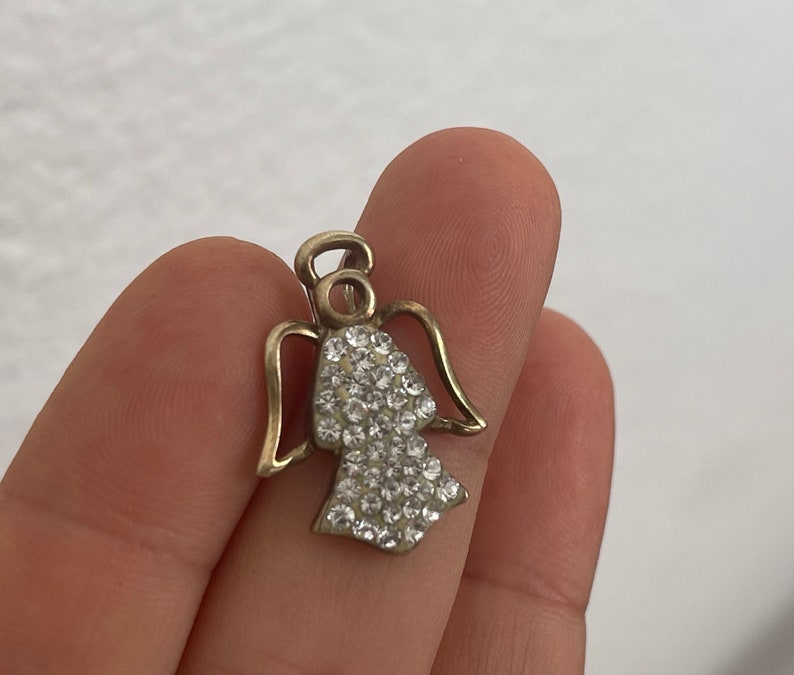 May include: A gold angel charm with clear crystal rhinestones. The angel has wings and a halo.