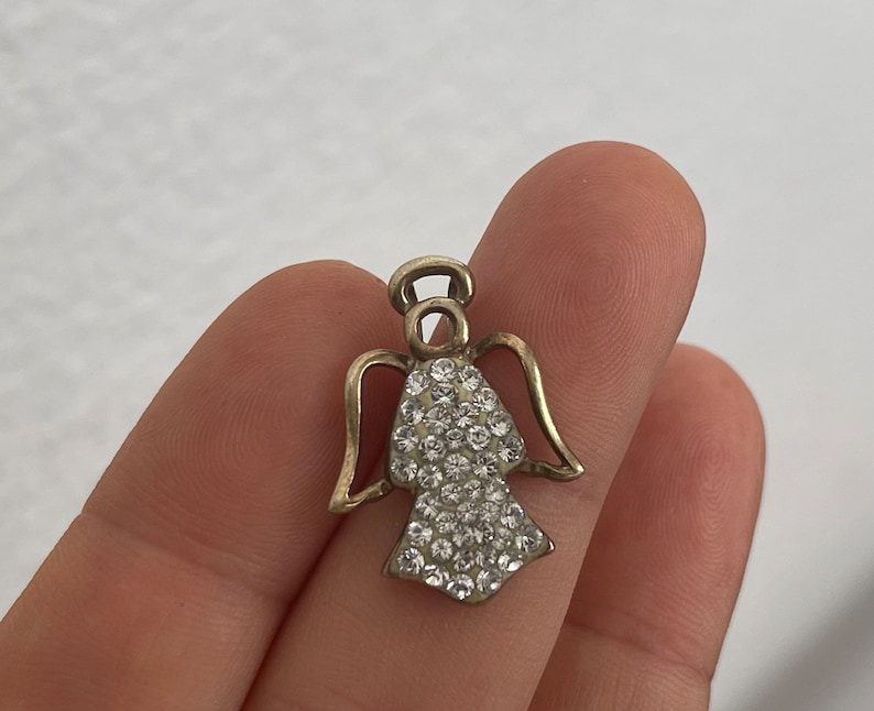 May include: A silver angel charm with a halo and wings, adorned with clear rhinestones.