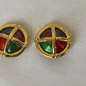 May include: A pair of gold tone earrings with a circular design. Each earring features four colored glass stones in a cross pattern.