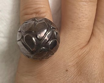May include: A silver ring with a textured, abstract design. The ring is round and has a three-dimensional appearance.