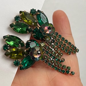May include: A pair of dangle earrings with green and gold accents. The earrings feature a cluster of green and gold rhinestones with a dangling chain of smaller green rhinestones.