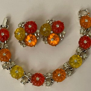 Könnte beinhalten: Ein Vintage-Armband und Ohrring-Set aus orangefarbenem, gelbem und rotem glasartigem Material und Strasssteinen in Blumenform. Das Set hat eine silberfarbene Metallbasis.