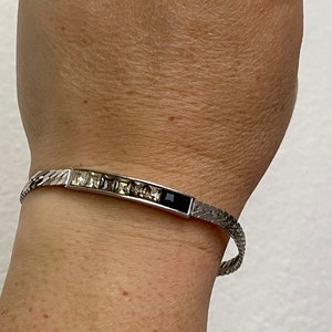 Puede incluir: Una pulsera de plata con una fila de piedras facetadas transparentes y una piedra negra en el centro.