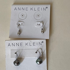 May include: Two pairs of earrings on white cards with the text "Anne Klein" printed on them. The earrings are silver with a pearl drop. One pair has a white pearl and the other pair has a dark gray pearl.