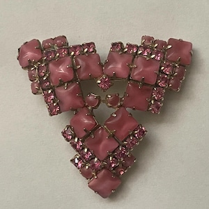 May include: A vintage brooch in a triangular shape, featuring a gold-tone metal setting. The brooch is adorned with pink square and round stones, and smaller pink rhinestones. The design is symmetrical and ornate.