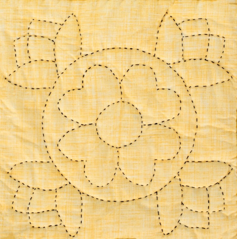 May include: A square, quilted fabric with a yellow background and a floral design. The design is created with black, dashed stitching, forming a large central flower and surrounding petal shapes. The fabric has a subtle, textured appearance.