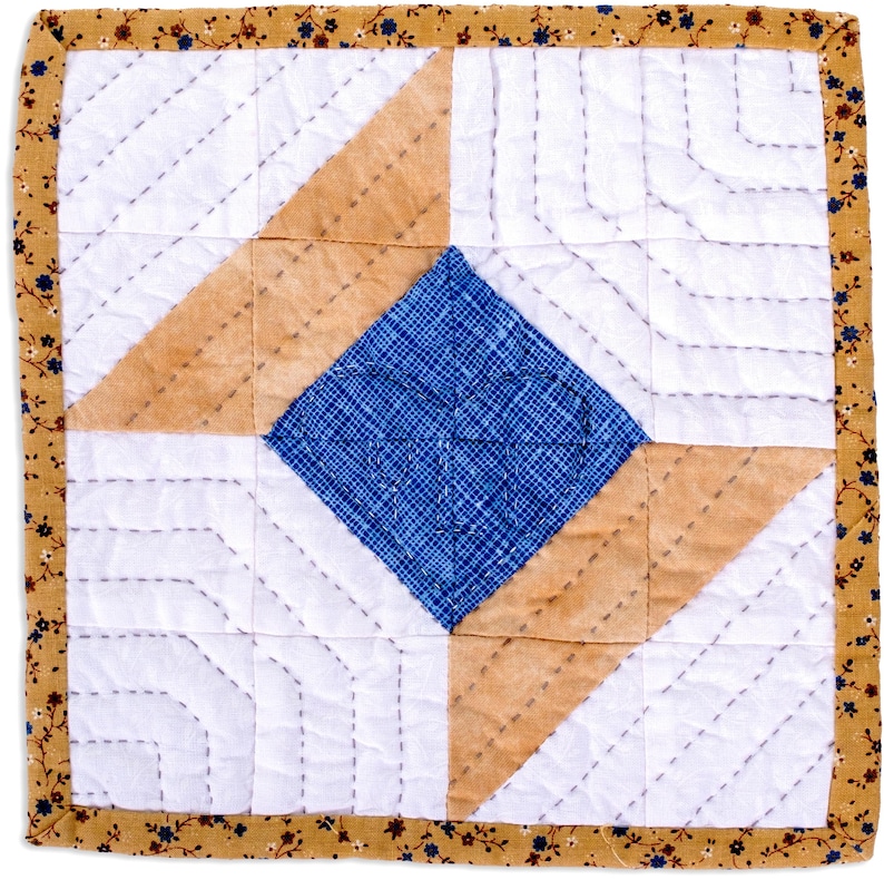 May include: Square quilted coaster with a central blue diamond, surrounded by tan and white geometric shapes. The edges are bordered with a floral patterned fabric in shades of brown, blue, and yellow. The stitching is visible.
