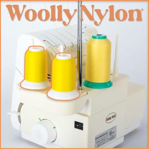 Op de afbeelding: Een crèmekleurige Baby Lock lockmachine met drie spoelen gele draad. De spoelen staan bovenop de machine, met de tekst "Woolly Nylon" in oranje bovenaan.