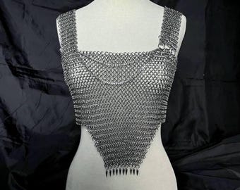 Könnte beinhalten: Ein silbernes Kettenhemd-Oberteil mit quadratischem Ausschnitt und Trägern. Das Kettenhemd besteht aus kleinen, ineinandergreifenden Metallringen. Der untere Teil des Oberteils hat ein spitzes Design mit kleinen Metallspitzen. Auf einer weißen Schaufensterpuppe.