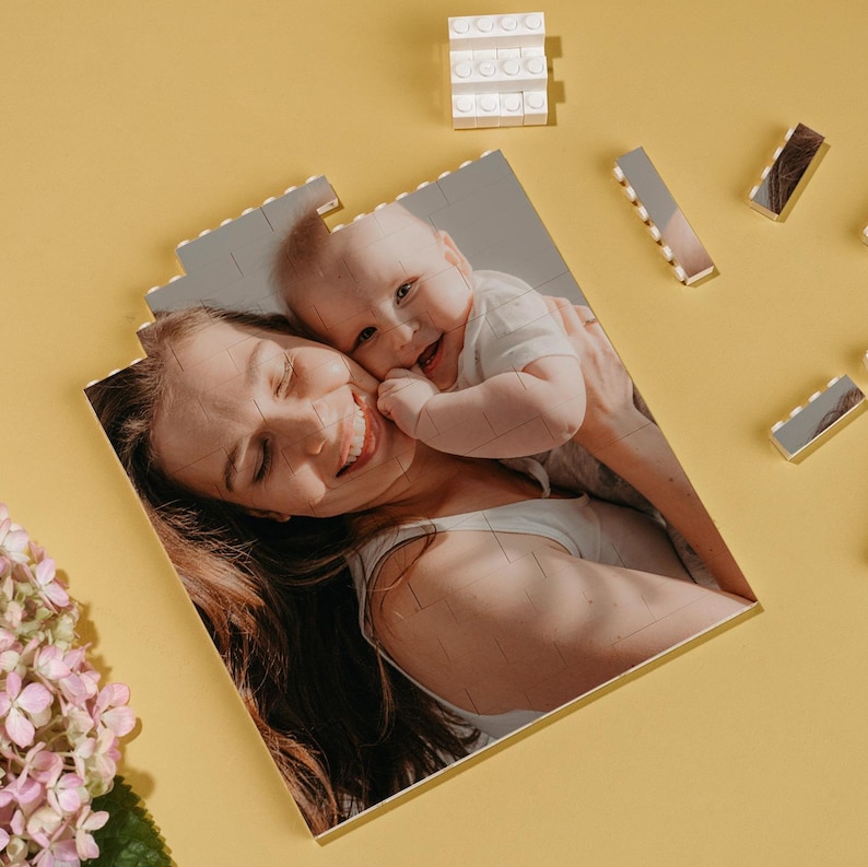 May include: A personalized photo puzzle featuring a smiling mother and baby. The puzzle is made of interlocking pieces, with a yellow background. Additional puzzle pieces and toy blocks are scattered around the puzzle.