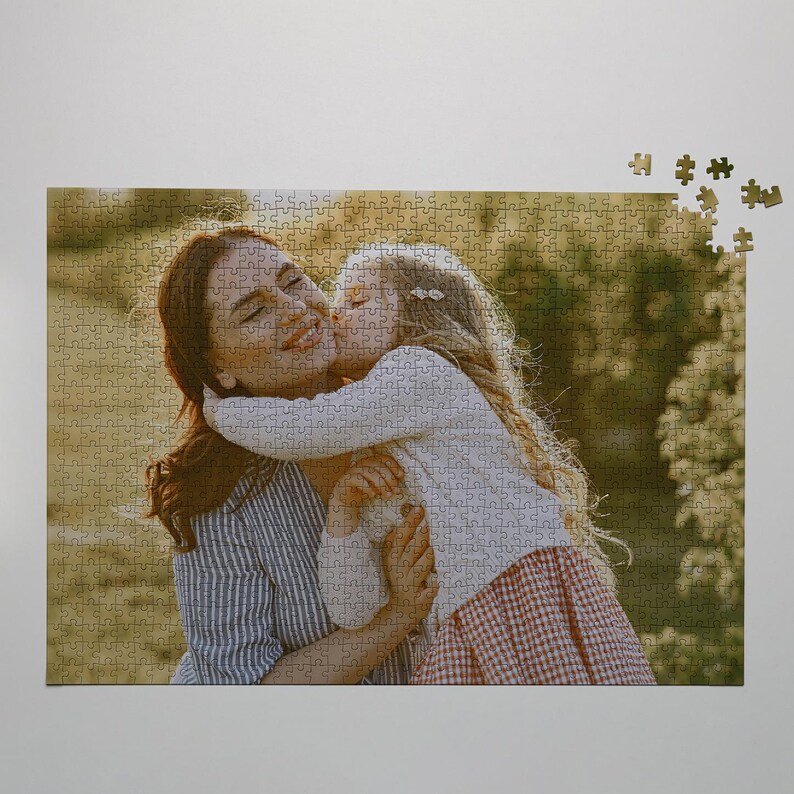 May include: A completed jigsaw puzzle featuring a photograph of a woman and a young girl embracing and kissing. The woman wears a blue and white striped shirt, and the girl wears a white sweater and a red and white checkered skirt. Some puzzle pieces are separate.