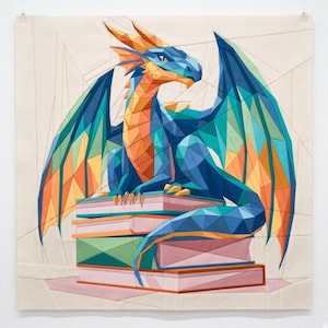 May include: A fabric wall hanging featuring a geometric, low-poly style dragon in shades of blue, orange, and teal. The dragon is perched atop a stack of books rendered in muted pink and green tones, all set against a plain, light-colored background.