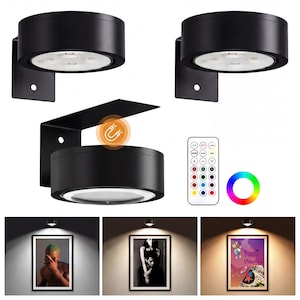 May include: Black LED wall-mounted spotlights. The image shows three spotlights, one with a magnetic bracket, a remote control, and a color wheel. The spotlights are illuminating framed artwork.
