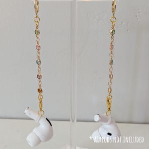 May include: Gold-colored AirPod earrings with a chain of colorful beads. The earrings have a gold clasp at the top and a gold charm to attach to the AirPod. The text "* AIRPODS NOT INCLUDED" is at the bottom right.