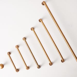 May include: A collection of seven gold-toned cabinet hardware pieces arranged in increasing size order. The set includes one round knob and six bar-style drawer pulls of varying lengths, all featuring a smooth, matte metallic finish.