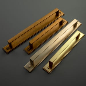 May include: Four metal door pulls in shades of gold and bronze. Each pull has a rectangular bar handle on a rectangular backplate. Finishes vary from dark, aged bronze to bright, polished gold. Ideal for cabinets or doors.