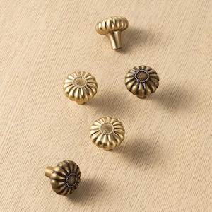 May include: Five round cabinet knobs with a metallic gold finish. Each knob features a fluted, pumpkin-like shape with a textured, circular center detail. The knobs are arranged in a scattered pattern, showing both top-down and side-angle views.