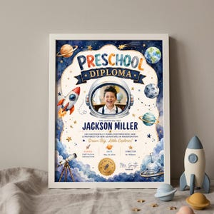 May include: A framed preschool diploma with a space theme. The diploma features a photo of a child in an astronaut helmet, the text "Preschool Diploma", and the child's name. Decorative elements include planets, stars, and a rocket.