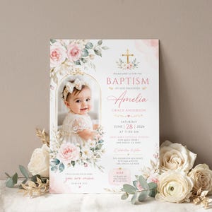 Könnte beinhalten: Eine Taufeinladungskarte mit einem Foto eines Babys in einem weißen Spitzenkleid und einem Blumenstirnband. Das Design zeigt rosa Rosen, grüne Blätter, ein goldenes Kreuz und den Text für die Taufe von Amelia Grace Anderson am 28. Juni 2026.