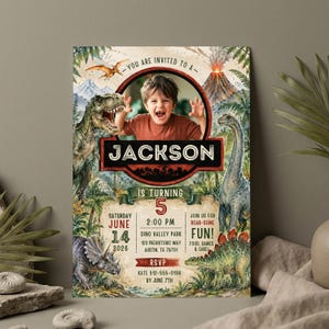 Op de afbeelding: Een gepersonaliseerde dinosaurus-thema verjaardagsuitnodiging met een foto van een kind, de naam "Jackson" en feestdetails. Het ontwerp bevat illustraties van dinosaurussen, een vulkaan en palmbomen. De tekst bevat "Je bent uitgenodigd voor..." en "Wordt 5."