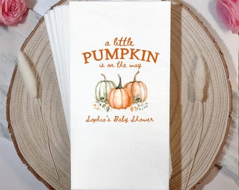 May include: White paper napkins with a pumpkin-themed baby shower design. The napkins feature the text "a little PUMPKIN is on the way" and the name "Sophia's Baby Shower" below a watercolor illustration of three pumpkins.