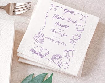 May include: White paper napkins with a purple illustrated design. The design includes the text "Ellie's Next Chapter" and other illustrations of books, a teapot, and flowers. A silver fork is visible in the upper left corner.