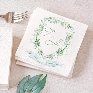 May include: White paper napkins with a floral design and the initials "T & H" in green. The napkins feature a light blue ribbon and the date "February 2026". A silver fork is visible in the background.
