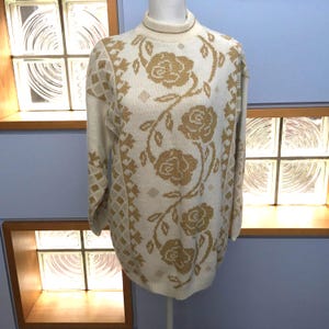 May include: A white sweater with a gold floral pattern. The sweater has a mock neck and long sleeves.