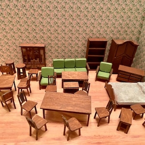 May include: A collection of miniature wooden dollhouse furniture including a sofa, chairs, tables, a bed with white bedding, a bookshelf, a cabinet, and a wardrobe. The pieces are crafted from brown wood, with some items featuring green fabric cushions.