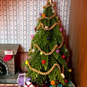 Puede incluir: Miniatura de árbol de Navidad decorado con adornos coloridos y una estrella dorada en la parte superior. El árbol está adornado con una guirnalda de cadena dorada y rodeado de regalos envueltos en varios colores. Una chimenea en miniatura con un calcetín está en el fondo.