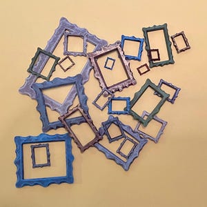 May include: A collection of various rectangular picture frames in assorted sizes and colors, including blue, green, purple, and bronze. The frames feature wavy, scalloped edges and are arranged in a scattered, overlapping pattern.