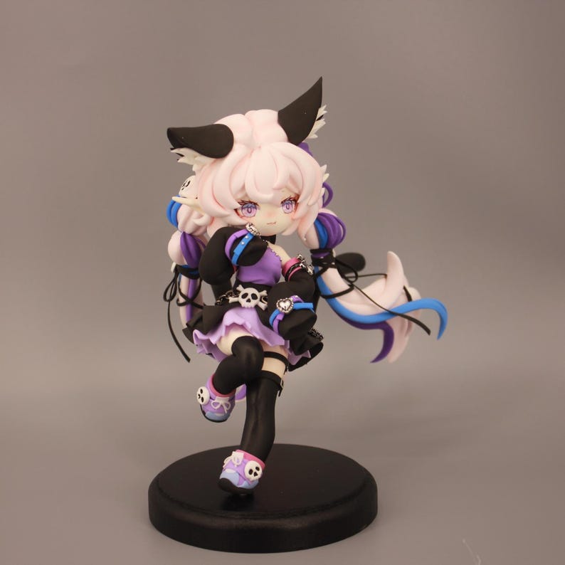 May include: A detailed figurine of a character with pink hair, black and white ears, and purple eyes. The figure wears a black and purple outfit with skull accents and black stockings. It stands on a black circular base.