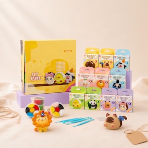 Könnte beinhalten: Ein Pet Tribe Bastelset mit lufttrocknender Knete, bestehend aus einer großen gelben Schachtel, mehreren kleinen Boxen mit Tierillustrationen, runden Behältern mit farbiger Knete, blauen Modellierwerkzeugen und zwei fertigen Knetfiguren.