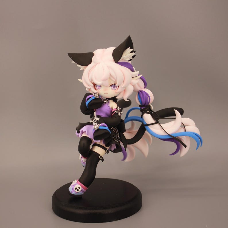 May include: A detailed figurine of a character with pink hair, black cat ears, and a purple and black outfit. The figure is posed dynamically on a black circular base, with a flowing tail and accents of blue and white.
