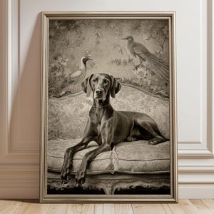Op de afbeelding: Sepia-getinte ingelijste prent van een Weimaraner-hond op een bloemenbank, met vogels op de achtergrond. Het kunstwerk wordt gepresenteerd tegen een witte muur en een houten vloer. De prent zit in een gouden lijst.