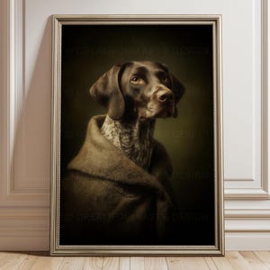 May include: A framed portrait of a German Shorthaired Pointer dog with brown and white speckled fur. The dog is wrapped in a thick, textured brown fabric draped over its shoulders, set against a dark, moody background within a metallic frame.