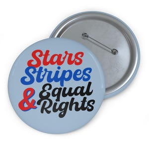 May include: A light blue button with the words "Stars Stripes & Equal Rights" in red, blue, and black. The button has a pin on the back and a silver rim. The button is a political statement.