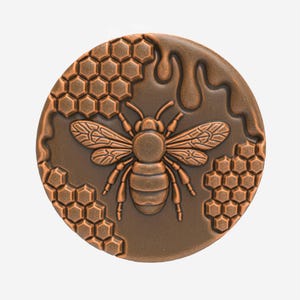 Può includere: Un elemento decorativo rotondo color bronzo con un'ape dettagliata con le ali spiegate. Il design include motivi a nido d'ape e un effetto miele gocciolante, creando un tema ispirato alla natura.