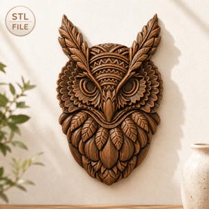 May include: A detailed, brown wooden owl wall art piece. The owl features intricate carvings of feathers, eyes, and geometric patterns. The image includes the text "STL FILE" in a circle in the upper left corner. The owl is displayed against a neutral background.