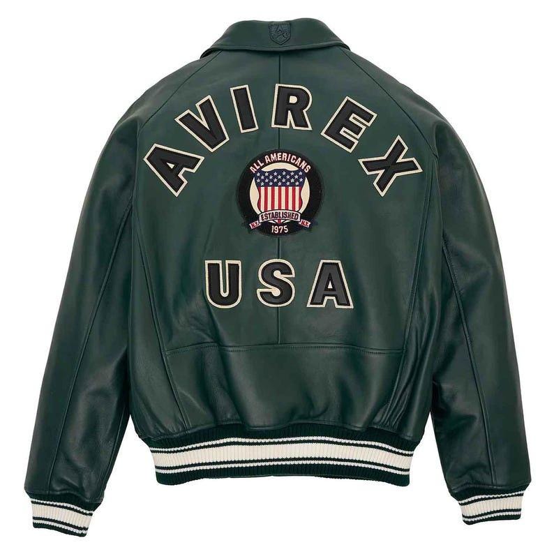 May include: A dark green leather bomber jacket with the word "AVIREX" arched across the upper back. Below the word "AVIREX" is a patch with the words "ALL AMERICANS" and "ESTABLISHED 1975" surrounding a US flag design. The word "USA" is below the patch.