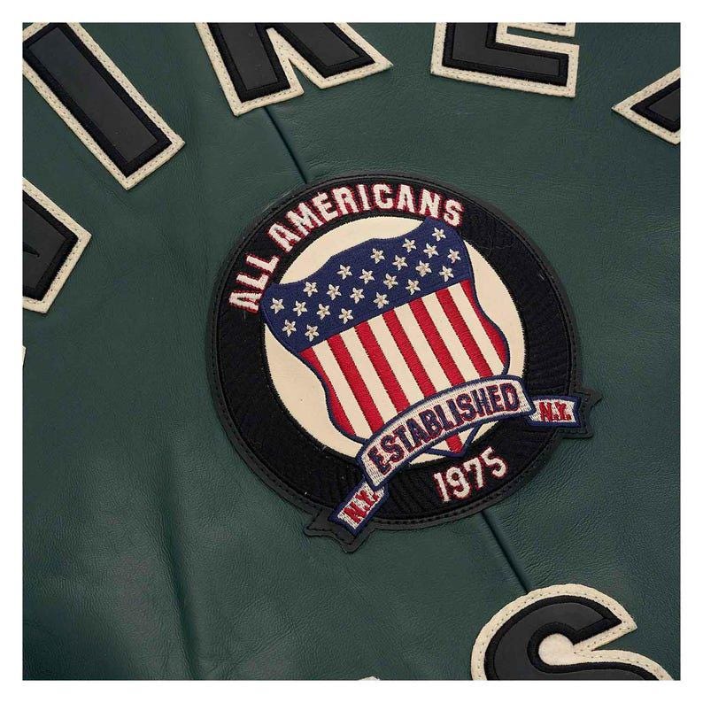 May include: Close-up of a dark green leather jacket with patches. The main patch features a shield design with the American flag and the words "ALL AMERICANS ESTABLISHED 1975 N.Y."