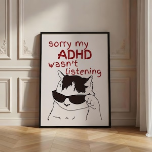 Peut inclure: Une affiche rectangulaire dans un cadre noir avec un fond blanc et le texte rouge sorry my ADHD wasn't listening. Sous le texte se trouve un dessin au trait noir et blanc représentant un chat portant des lunettes de soleil et touchant son oreille.