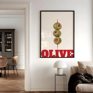 May include: A framed vertical wall art print featuring a centred illustration of three green olives with red pimento centres stacked on a wooden toothpick. The word OLIVE is printed in large, bold, red capital letters at the bottom of the print.