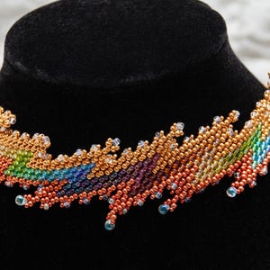 Può includere: Una collana di perline colorate con un motivo arcobaleno e accenti dorati. La collana è esposta su un manichino di velluto nero.