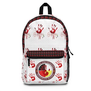 May include: A white backpack featuring a repeating red handprint pattern and a central circular emblem with the text "MISSING AND MURDERED INDIGENOUS WOMEN" surrounding a red handprint over a black, red, and yellow background with black trim.