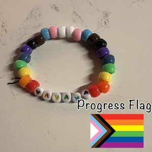 May include: A beaded bracelet featuring a rainbow of colors, including red, orange, yellow, green, blue, purple, black, brown, pink, and white. Some beads have heart-shaped designs. The text "Progress Flag" is visible.