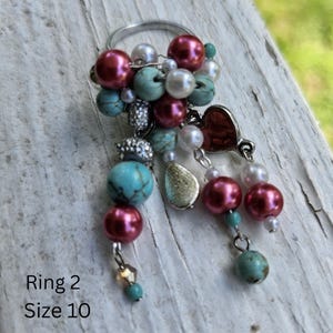 May include: A silver ring with a cluster of beads in shades of turquoise, burgundy, and white. The ring features a heart charm and the text "Ring 2 Size 10".