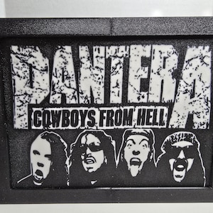 May include: Black framed artwork featuring the band Pantera. The band's name is displayed in white, distressed lettering above the text "Cowboys From Hell." Below the text are four black and white portraits of the band members.